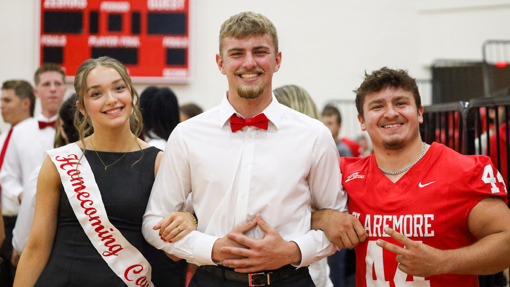 Three smiling students pose together, including a Homecoming Court representative and a Claremore football player.