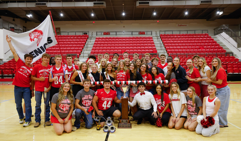 Claremore High School students gather around the Homecoming trophy in the gym, wearing red and white Zebra gear.