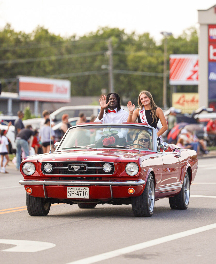 Two Homecoming Court representatives wave from a red Mustang convertible.