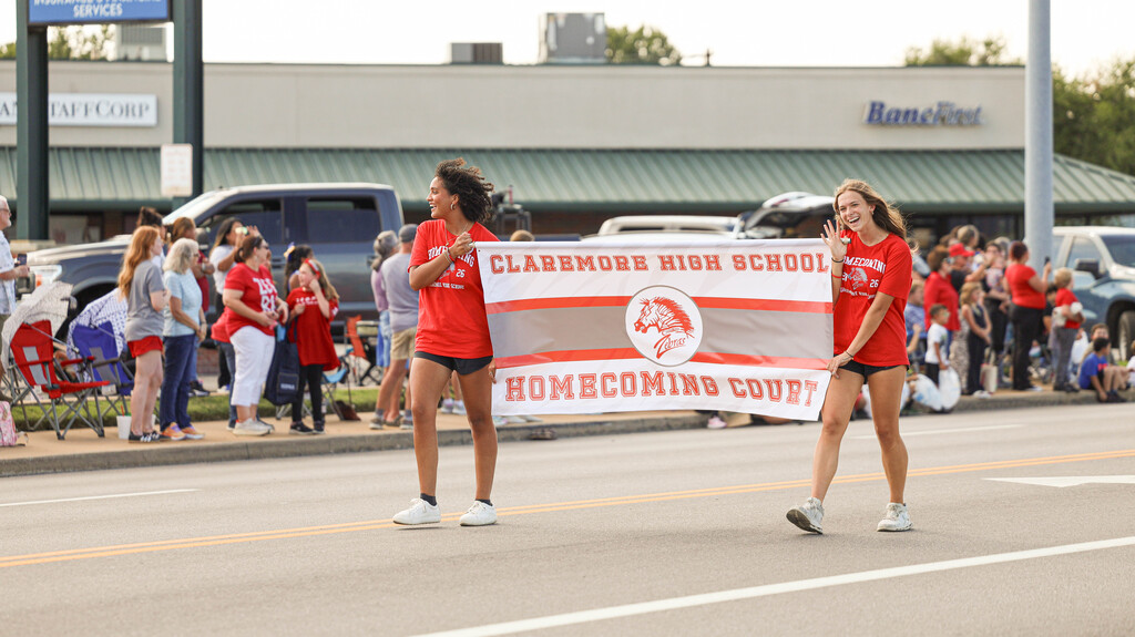 Two students carry the Claremore High School Homecoming Court banner.