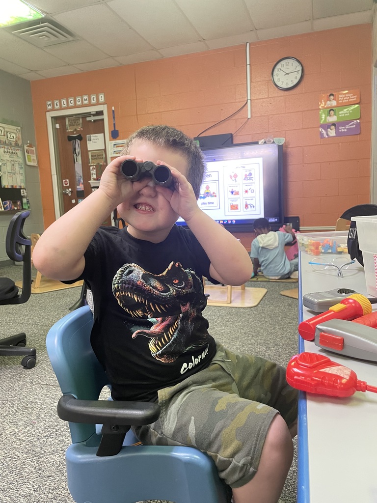 student looking through binoculars and is wearing a dinosaur shirt