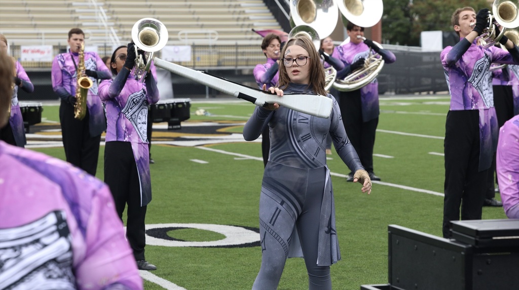 A color guard member performs with a rifle as the Zebra Band plays behind her.