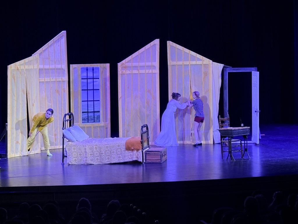 CHS drama students perform a scene on a bedroom set under purple lighting.