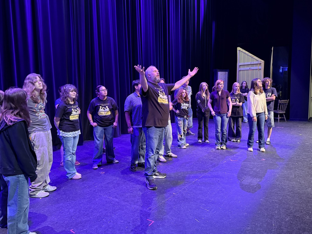 A teacher works with drama students during a rehearsal on stage.