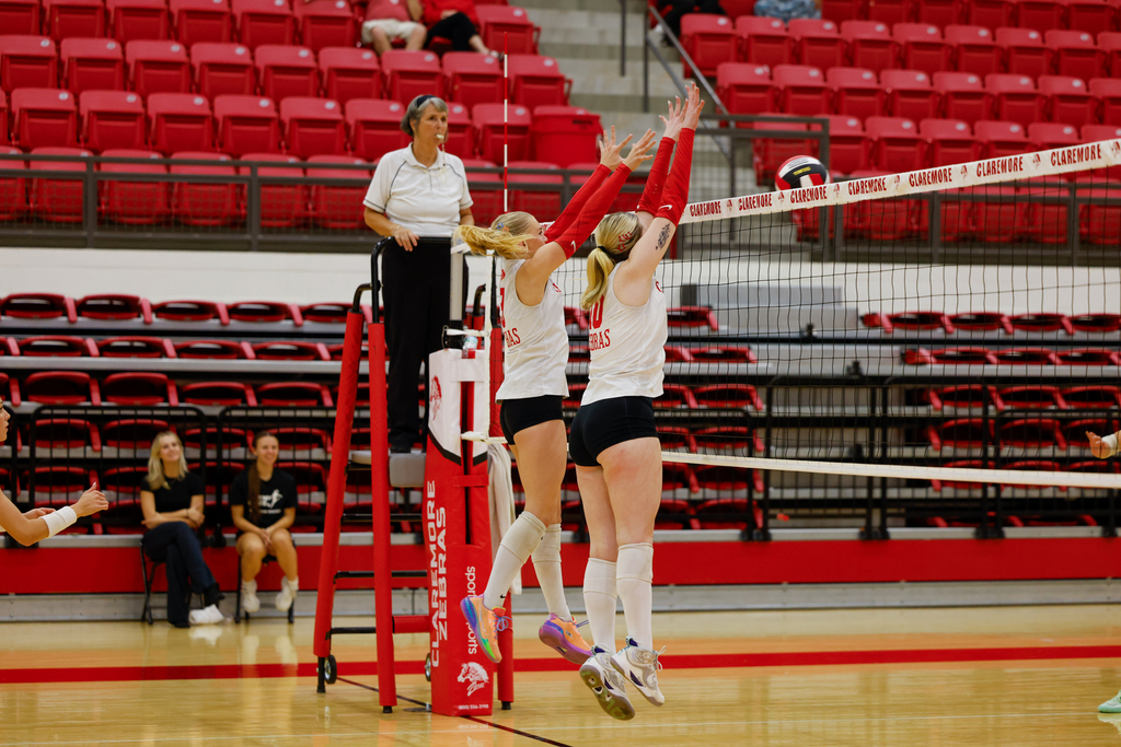 Two Lady Zebra volleyball players jump to block a ball at the net.