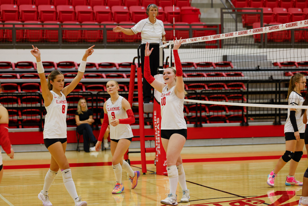 Claremore volleyball players celebrate a point with their hands raised.