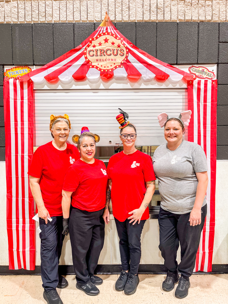 Four Claremont Child Nutrition employees pose in circus-themed accessories beneath a red-and-white circus tent decoration.