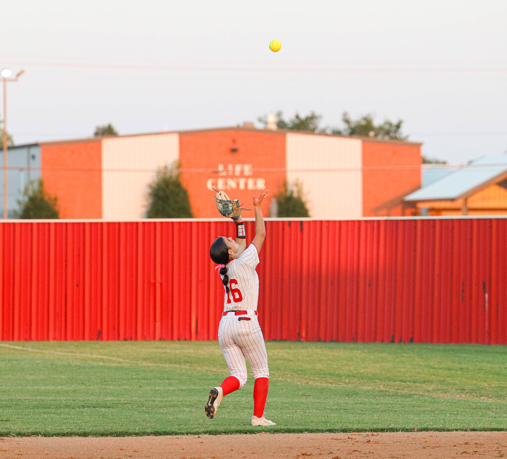 Claremore softball player reaches up to catch a fly ball in the outfield.