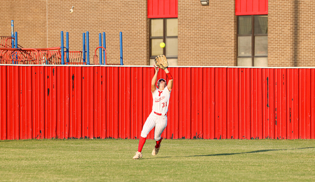 Claremore softball player reaches up to catch a fly ball in the outfield.