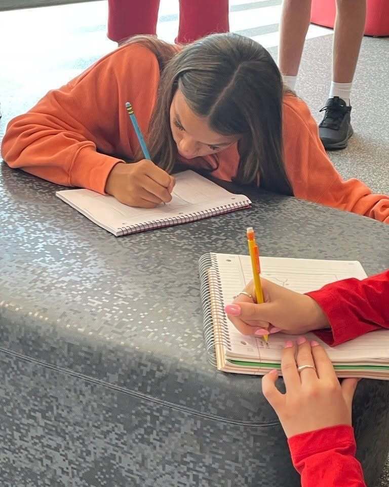 Two students writing in notebooks while working together.
