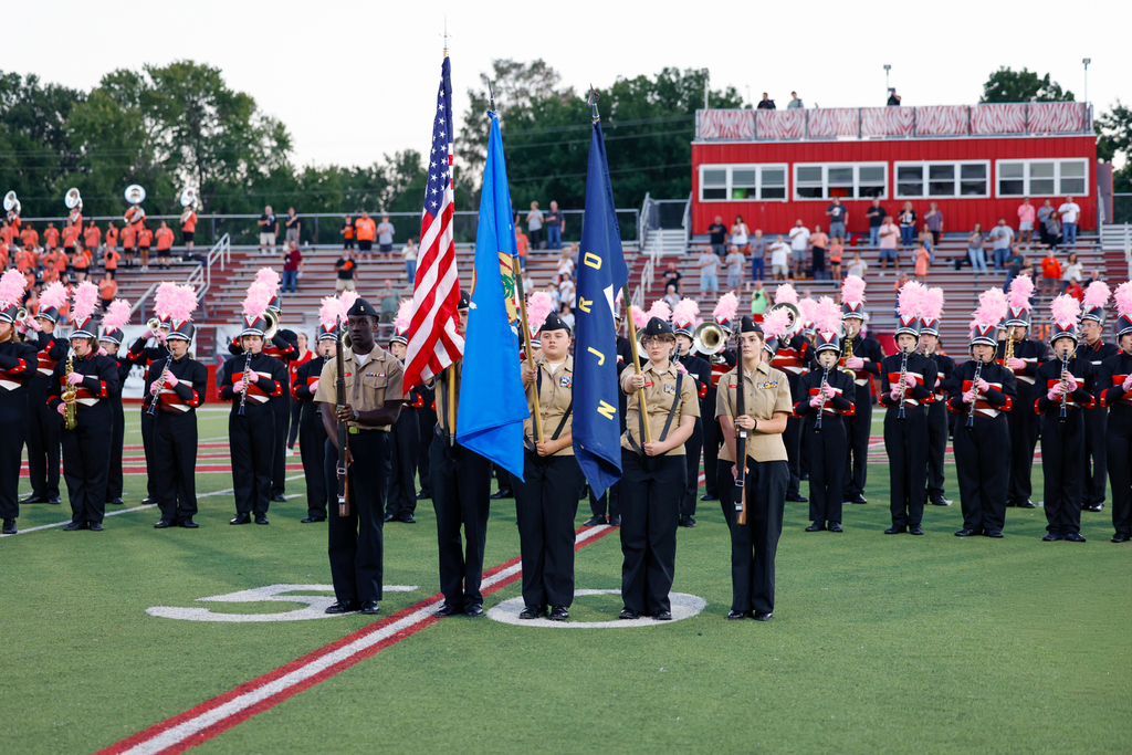 Claremore NJROTC cadets present the flags at midfield in front of the Zebra Band wearing pink plumes.