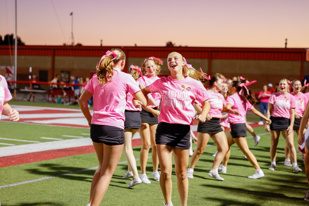 Claremore cheerleaders in pink shirts and dancing together on the football field.