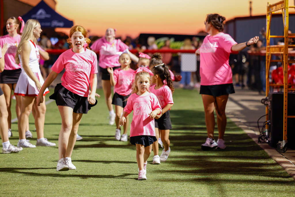 Young cheerleaders wearing pink shirts perform on the sidelines during Pink Out Night.