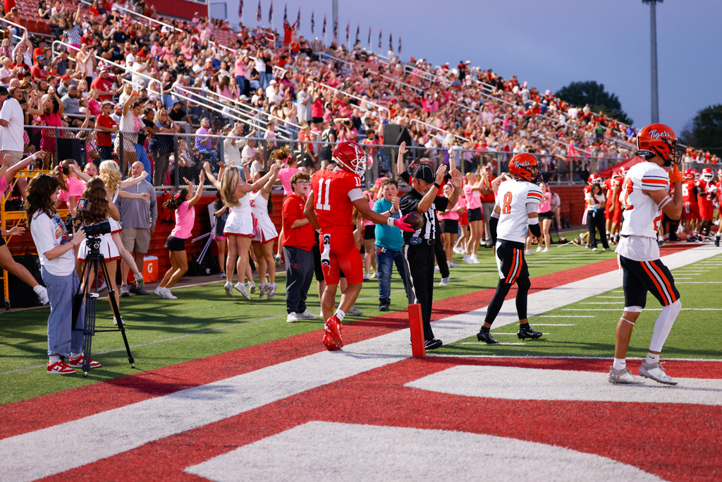 A Claremore football player celebrates near the end zone as fans and cheerleaders cheer behind him.