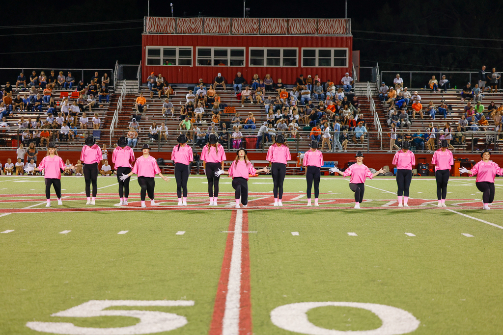 Claremore dance team members perform at midfield in pink shirts and black pants.