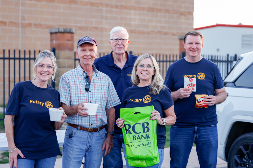 Five community members, several wearing Rotary Club shirts, pose together while holding chili bowls and sponsor items at the annual Chili Supper.