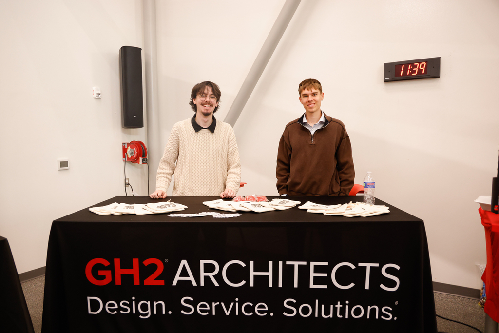 Two GH2 Architects representatives stand behind a table with promotional materials.