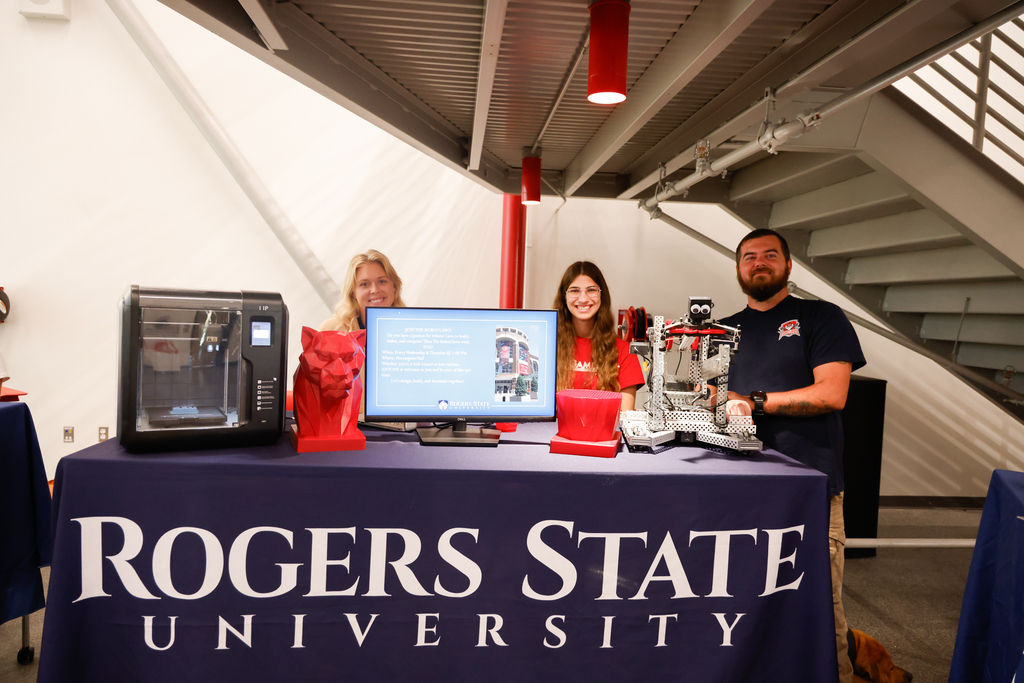Three RSU representatives stand behind a display featuring a robot and 3D printer.