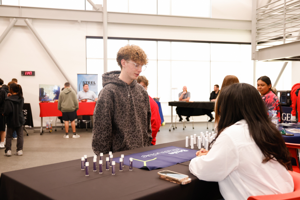 A student talks with a representative at a table displaying career information.