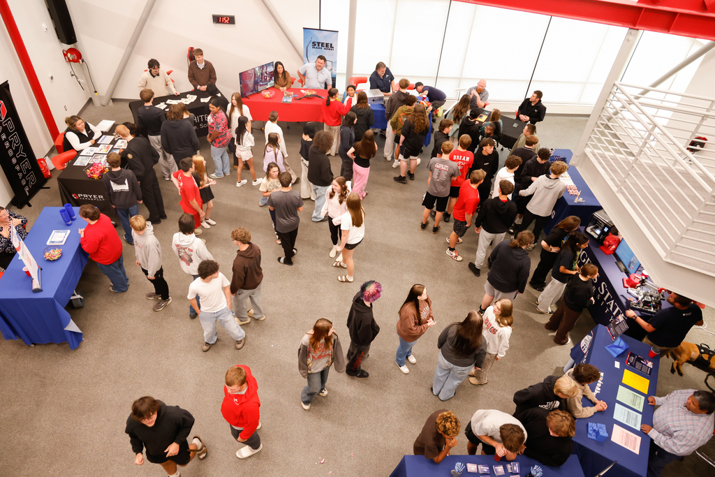 An overhead view shows students visiting booths and talking with industry representatives.