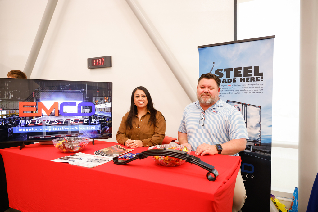 Two EMCO Industries representatives stand behind a table displaying company materials and products.