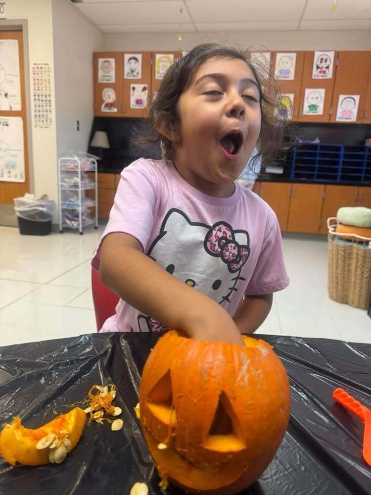 A student reacts with surprise while scooping out pumpkin guts.