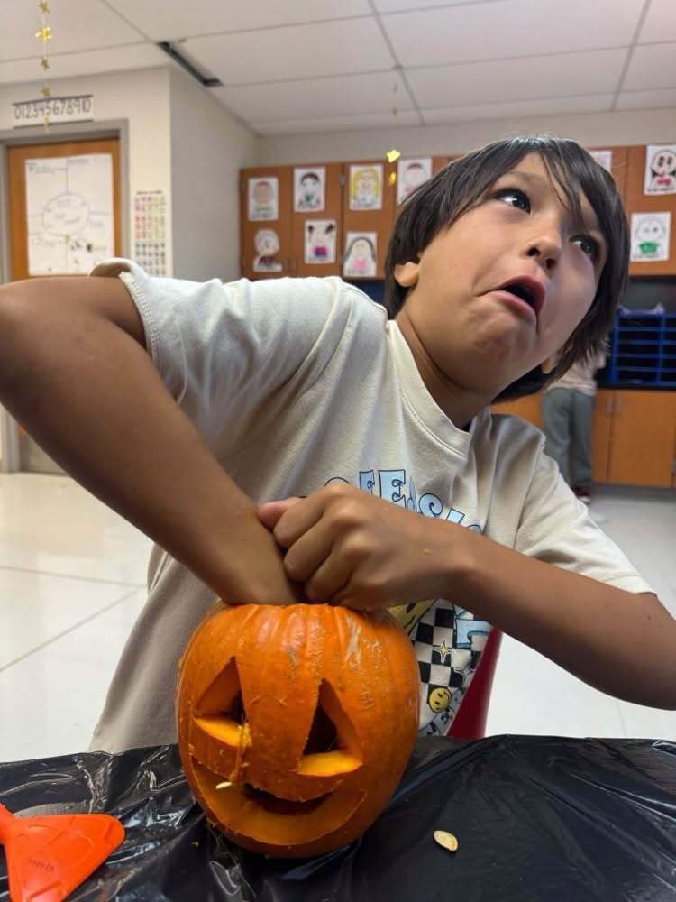 A student makes a funny face while pulling seeds and pulp from the pumpkin.