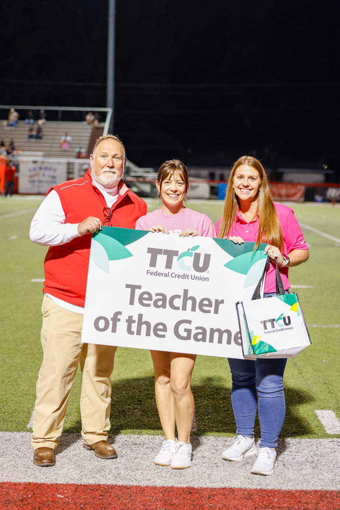 Superintendent Bryan Frazier, Kylie James, and CHS Principal Mrs. Lee smile while holding the TTCU Teacher of the Game sign on the football field.
