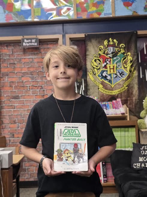student wearing a black shirt, holding a book titled jedi academy
