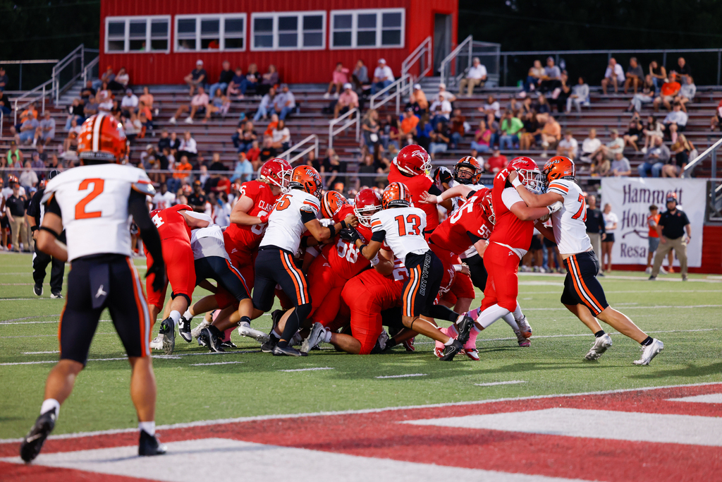 Claremore players in red uniforms battle opposing players at the line of scrimmage.