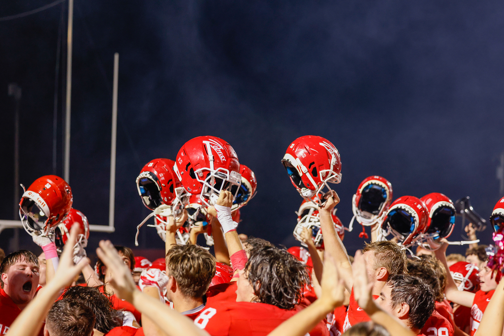 Claremore football players raise their helmets together during a postgame celebration.