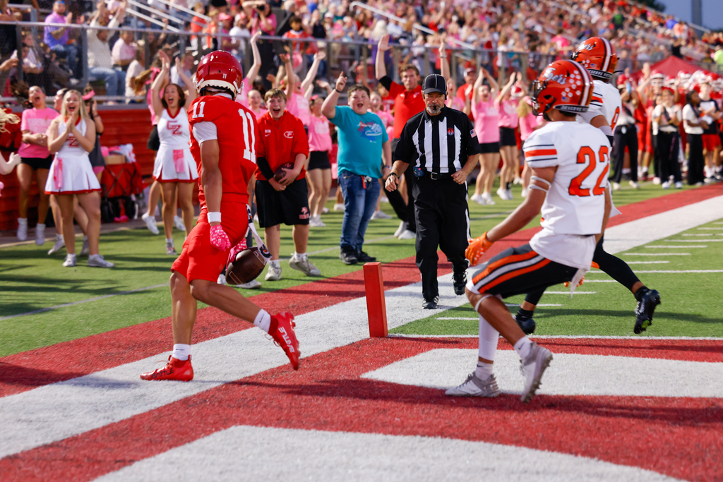 Claremore player #11 celebrates in the end zone as fans and cheerleaders cheer behind him.