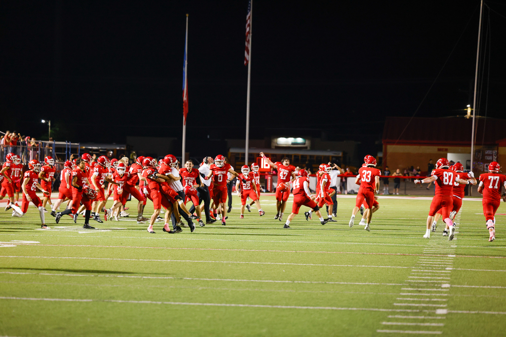Claremore players celebrate on the field, with teammates jumping and cheering.