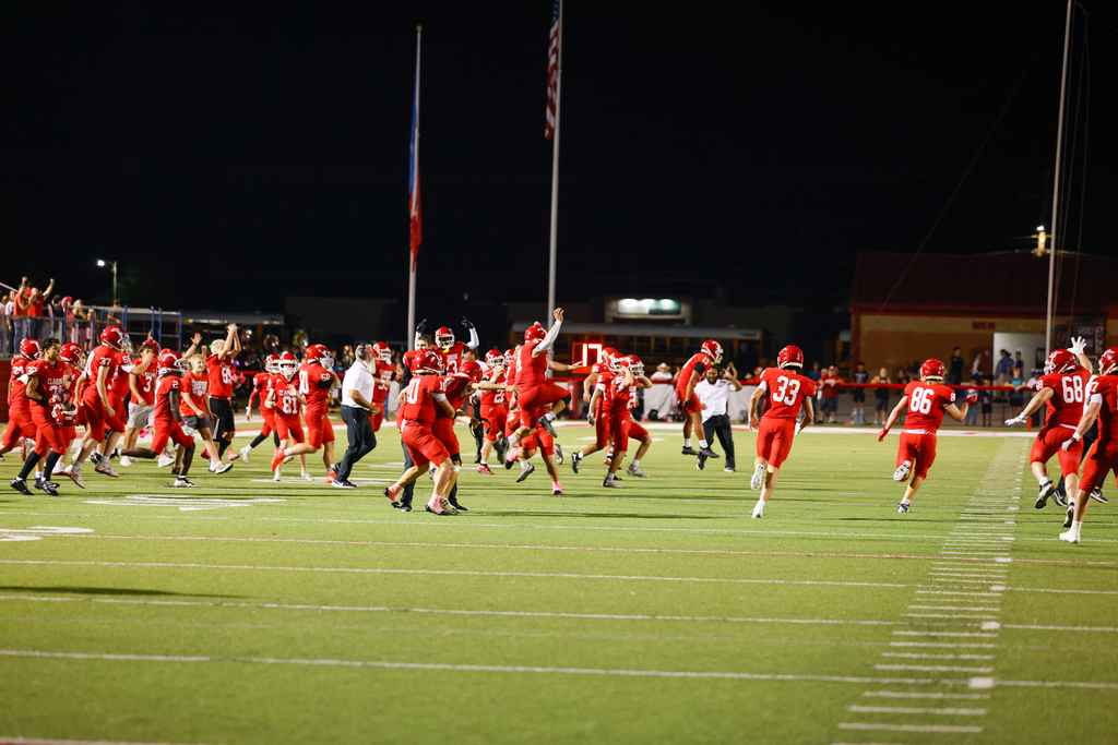 Claremore football players and coaches run across the field celebrating a victory.