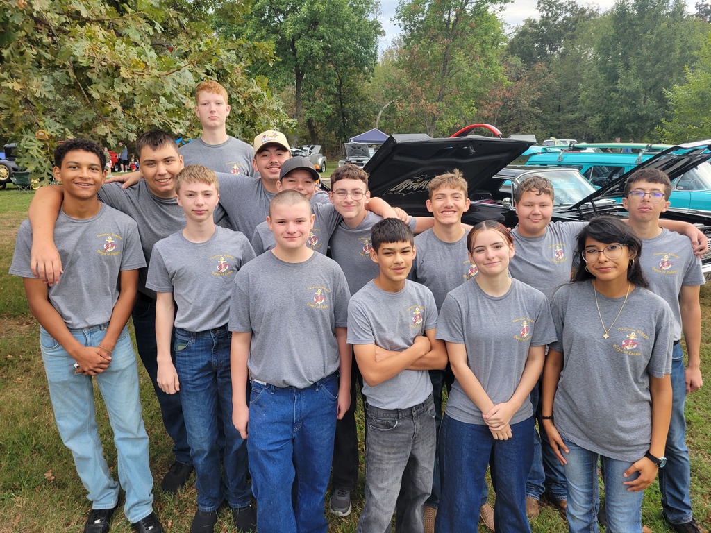 NJROTC cadets gather for a group photo in front of classic cars at the car show.