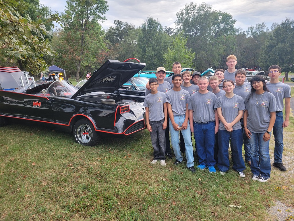 Claremore NJROTC cadets pose beside a black and red Batmobile with its hood raised.