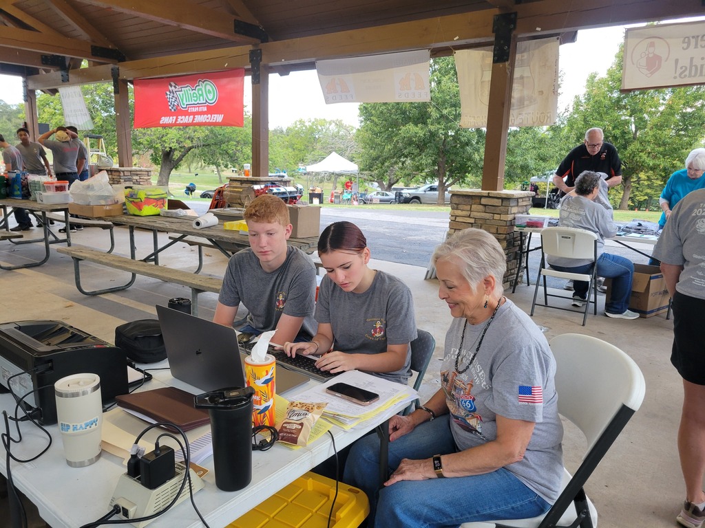 Two Claremore NJROTC cadets work on a laptop alongside a volunteer at the car show registration table.