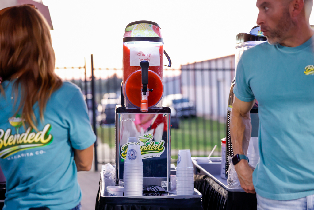 Blended Margarita Co. team members stand beside a Cherry Bomb slushie machine with Armstrong Bank cups ready for fans.