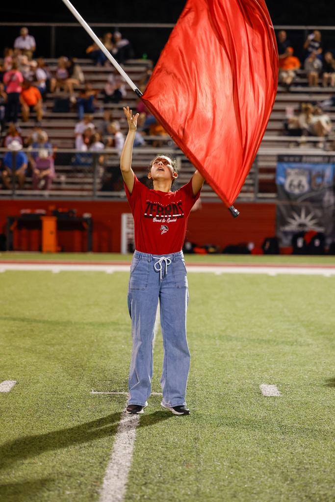 A color guard member in a red Zebra Band shirt reaches upward beneath a large red flag.