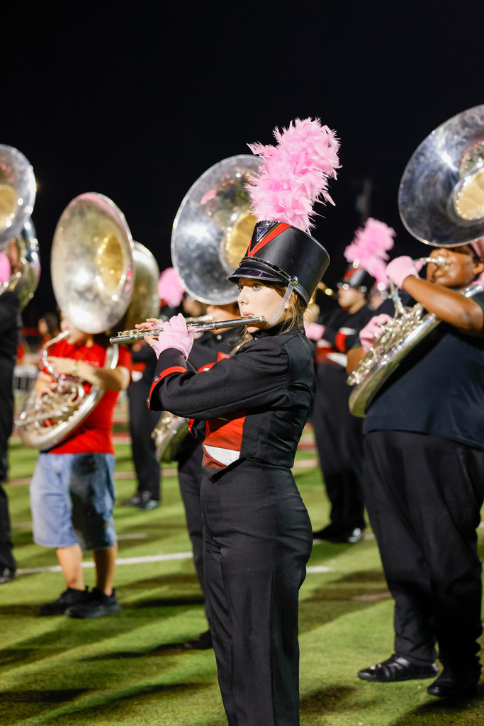 A Zebra Band member in uniform plays the flute with sousaphone players behind her.