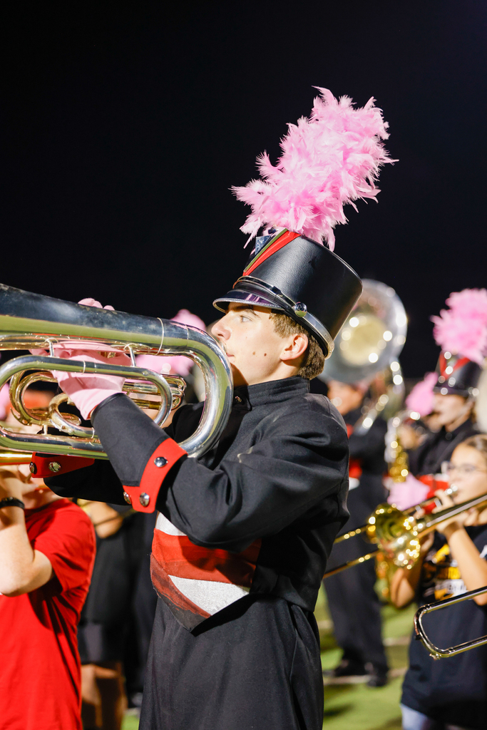 Close-up of a Zebra Band member playing a brass instrument while wearing a black uniform with a pink plume.