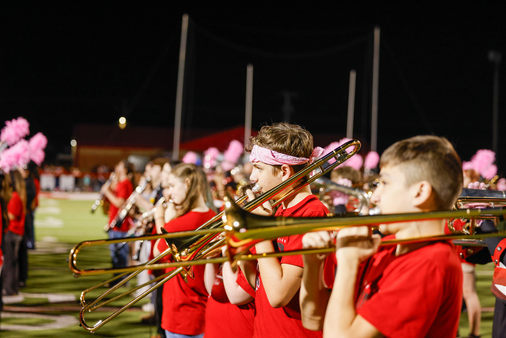 Young musicians in red shirts play trombones together on the football field.