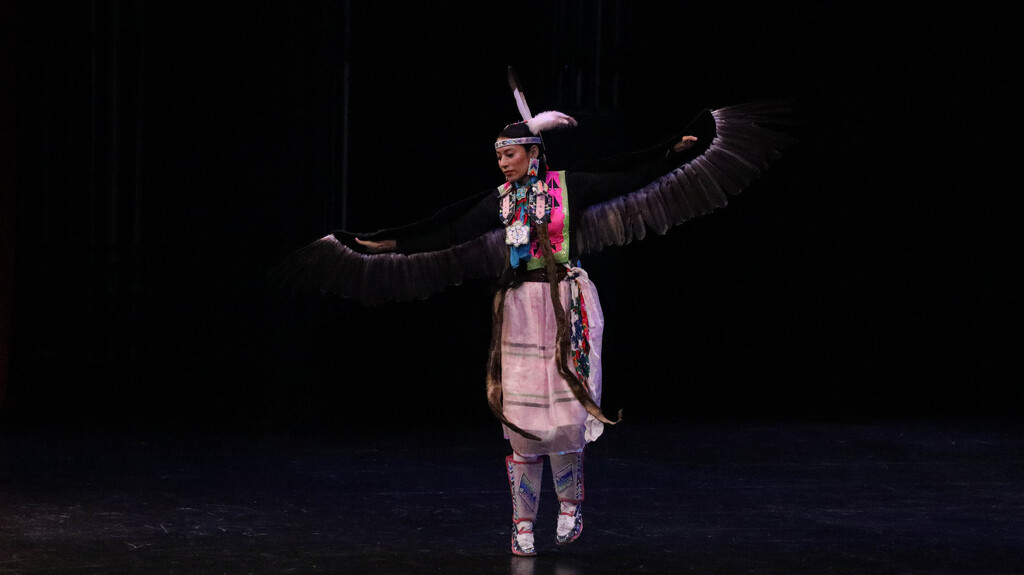Female Rising Buffalo dancer performing with feathered wings extended.