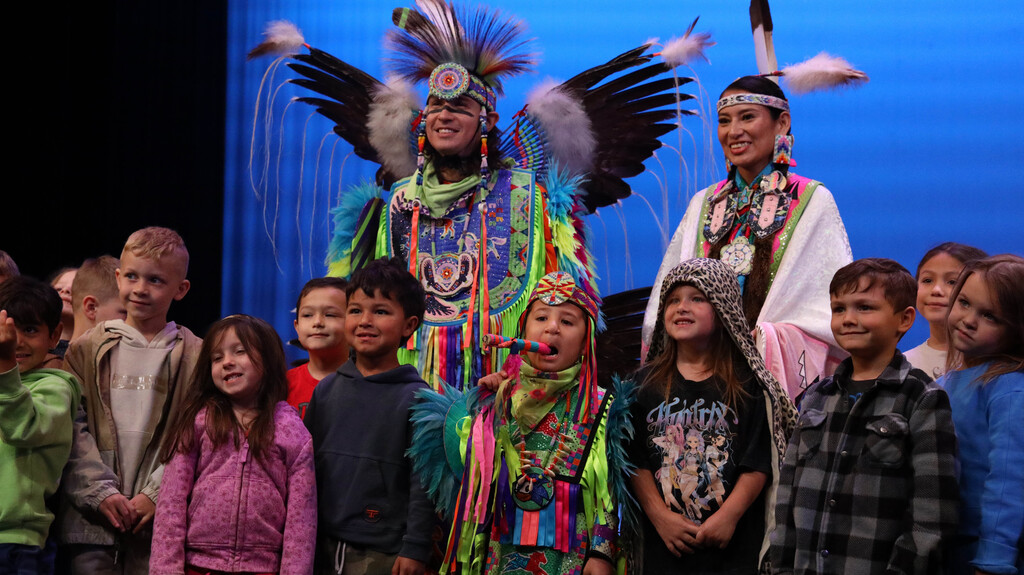Rising Buffalo dancers posing with elementary students on stage.