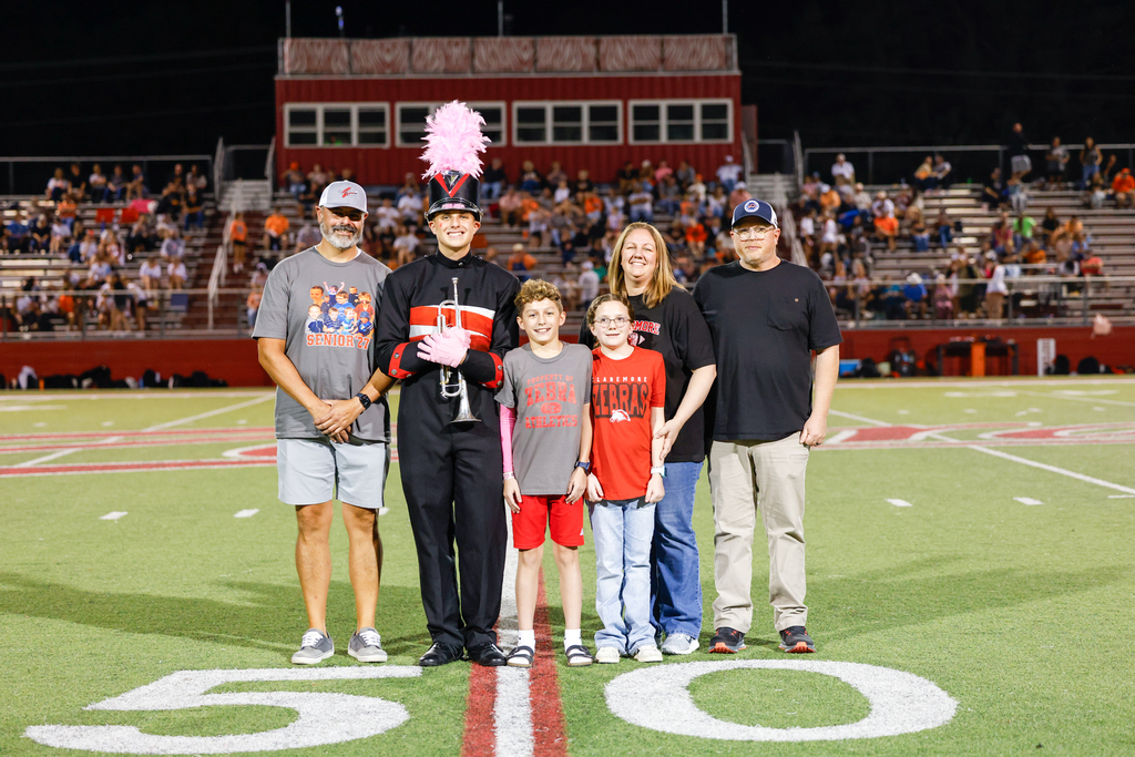 Senior Zebra Band trumpet player in uniform poses with five family members at midfield.