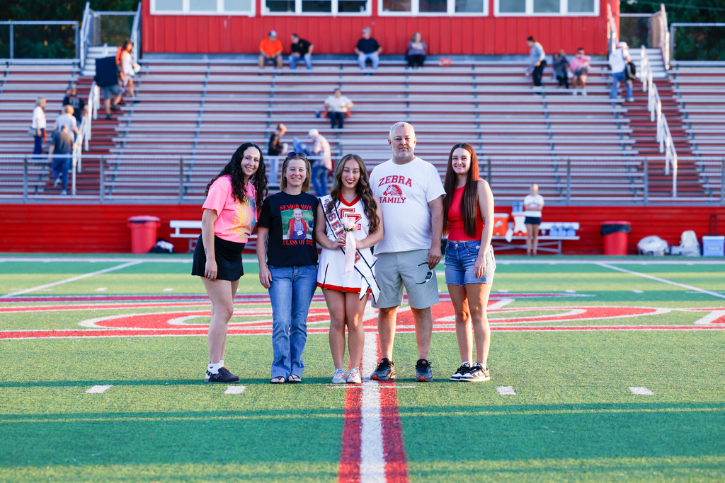 Senior cheerleader in uniform holds flowers while posing with four family members on the football field.