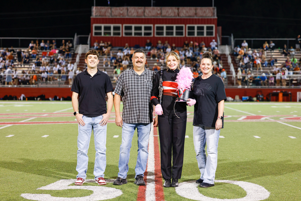 Senior Zebra Band member in uniform holds a clarinet and marching hat while posing with three family members.