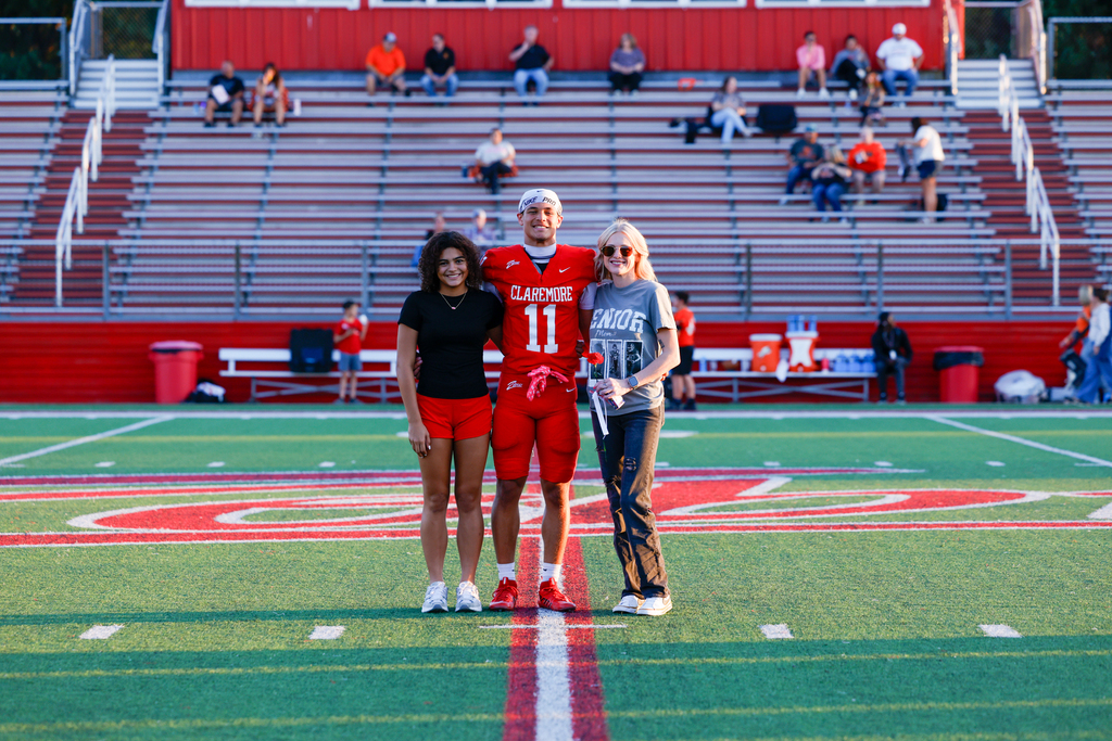 Claremore football player #11 smiles with two family members at midfield during Senior Night.