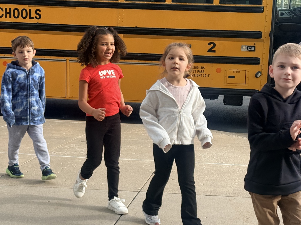 Four elementary students walk along the sidewalk in front of a Claremore Public Schools bus.