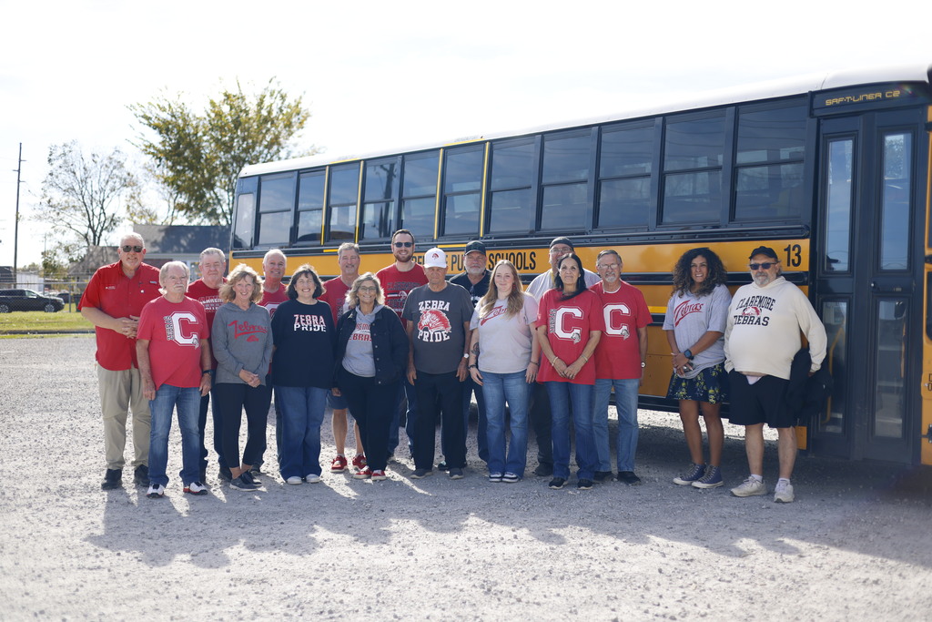Claremore Public Schools transportation staff pose together in front of a yellow school bus.